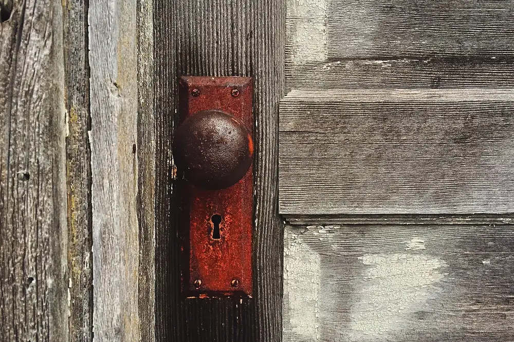 Weathered antique door knob and keyhole plate on an aged wooden door, the kind of original hardware found on older Sacramento homes