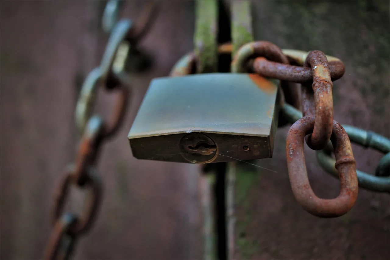 A closed padlock hanging from a rusted chain on a metal gate